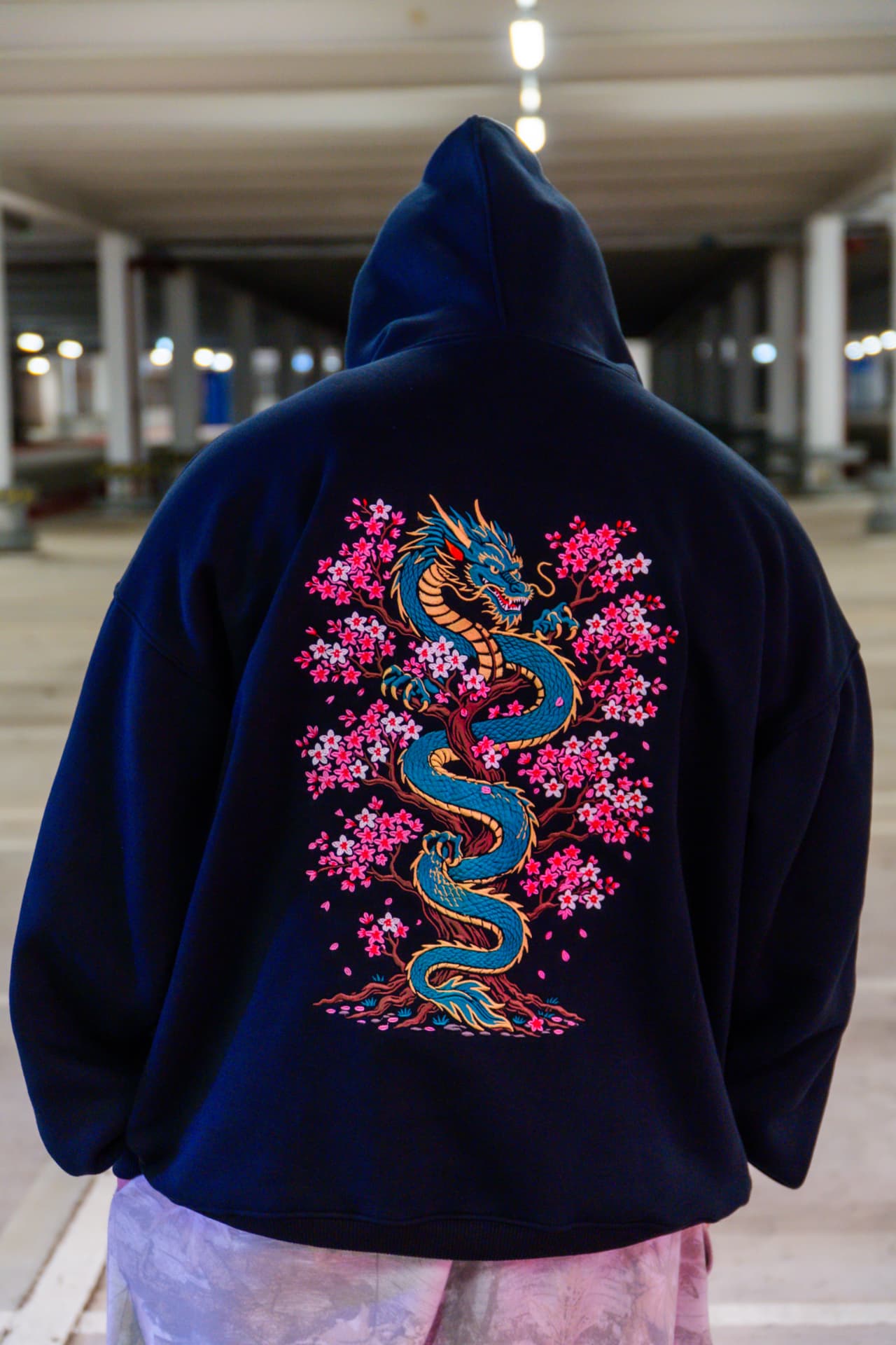 Sakura Dragon back print — model wearing black heavyweight hoodie with emerald dragon and sakura embroidery
